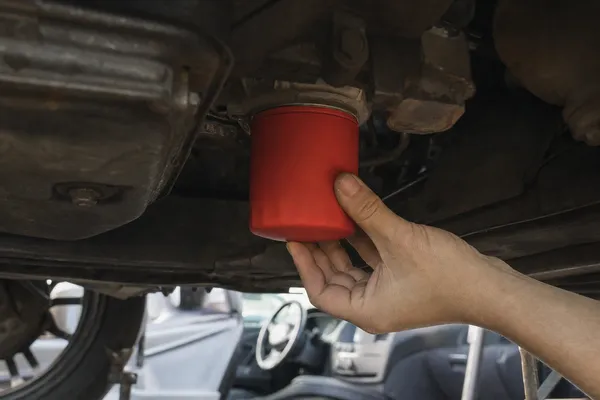 A hand checking a freshly fitted red oil filter under the engine for leaks